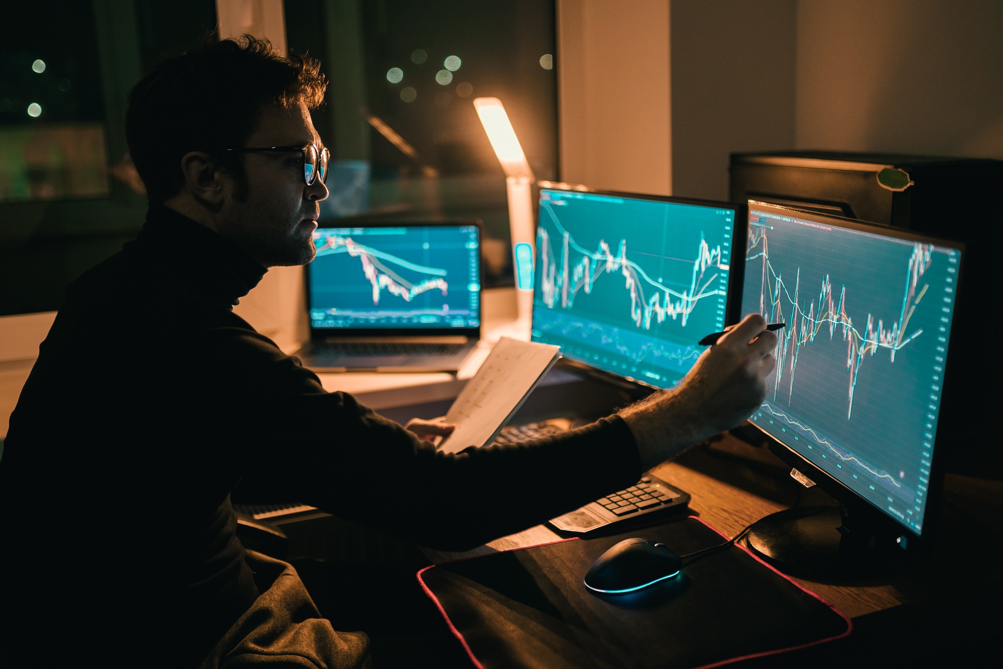 Analyzing the Market In a dimly lit home office, a male trader reviews charts and indexes